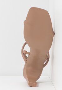 Sandale beige à talon haut avec fines lanières et bout carré, vue de la semelle face à la caméra sur fond blanc.