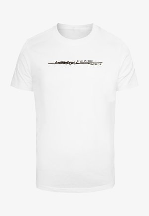 Bela kratka majica s kratkimi rokavi, ki ima črn napis "ŽIVI V TRENUTKU" z vodoravno linijo zasnove nad njim.