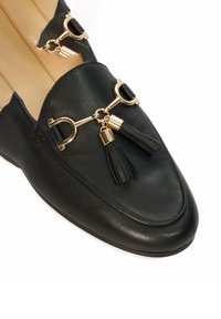 Black leather loafers featuring a gold-toned hardware accent with tassels. Smooth texture, rounded toe, and a low heel.