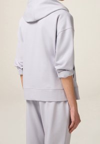 Felpa grigia chiara con una vestibilità comoda, dotata di cappuccio, spalle scese e orlo a coste. Realizzata in morbido tessuto misto cotone.