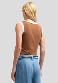 Brązowy bezrękawnik z białym teksturowanym kołnierzykiem, połączony z jasnoniebieskimi spodniami o wysokim stanie z paskiem w paski.