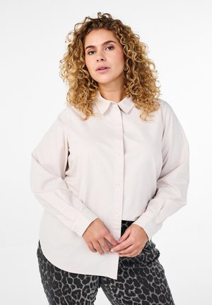 Camicia button-up beige chiaro realizzata in un tessuto morbido, con colletto e maniche lunghe, abbinata a pantaloni scuri con stampa leopardata.