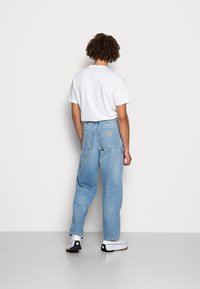 Lys blå høyt midje jeans med en avslappet passform, med to baklommer og en synlig merkeetikett. Kombinert med en enkel hvit t-skjorte.