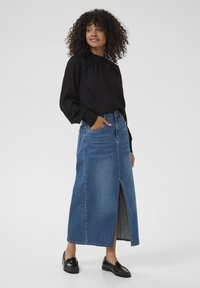 Denim maxi skirt with a front slit, featuring a high waist and two side pockets. Paired with a black long-sleeve top and glossy black loafers.