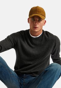 Un pull gris foncé à col rond, associé à un jean en denim bleu et une casquette en velours côtelé moutarde. La texture du tissu semble douce et lisse.