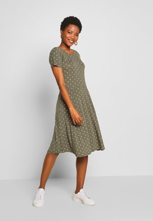 Olive green dress with short sleeves, white polka dots, flared skirt, and crew neckline, paired with white sneakers for a casual look.