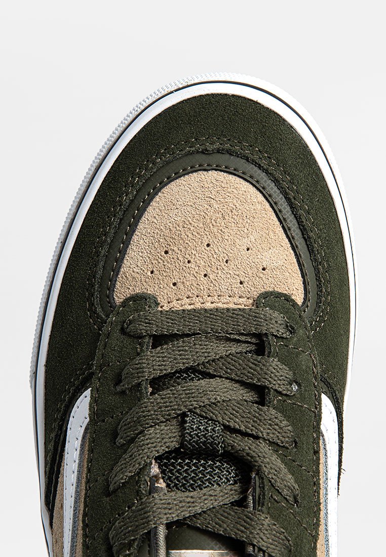 Zapatilla de ante verde y cuero beige con superficie texturizada, punta redonda, suela blanca y cordones oscuros. Presenta una franja blanca lateral.