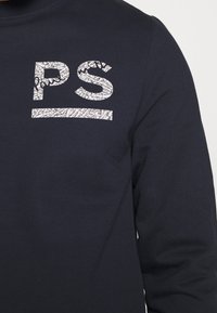 Camisa de manga larga azul marino con un logo blanco texturizado "PS" en el pecho. Material de algodón con una textura suave.