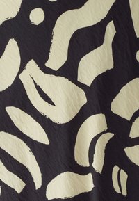 Czarna tkanina z dużymi, abstrakcyjnymi białymi kształtami, w tym falistymi liniami i okrągłymi plamami, o teksturowanej, lekko pogniecionej powierzchni.