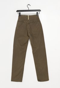 Hnědé kalhoty s vysokým pasem a zadními kapsami visící na černém ramínku na bílém pozadí.