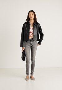 Czarna skórzana krótka kurtka z kołnierzem, noszona na topie w stylu tie-dye, zestawiona z jasnoszarymi obcisłymi jeansami i zdobionymi balerinami, trzymająca torebkę w groszki.