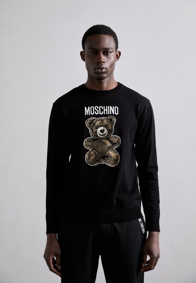 Hanorac negru cu mâneci lungi, având un grafic cu un ursuleț de pluș în tonuri de maro și negru, cu textul "MOSCHINO" deasupra. Material moale, design ajustat.
