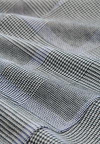 Tkanina s tkaným vzorem houndstooth v černé, bílé a modré barvě. Hladký povrch se jemným leskem a vrstvenými záhyby.