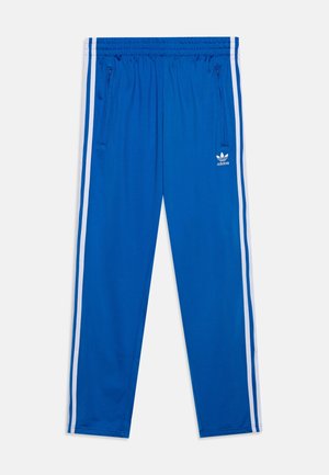 Pantaloni da ginnastica Adidas blu con strisce laterali bianche, vita elasticizzata, tasche con cerniera e logo Trefoil di Adidas sulla coscia destra.