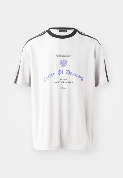 T-shirt à rayures blanches avec col rond noir, arborant un texte bleu et un design graphique. Coupé classique avec des manches courtes et des rayures latérales.