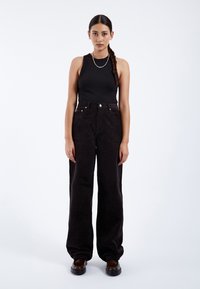 Top de tirantes negro acanalado combinado con pantalones de pana de pierna ancha y cintura alta. Detalles destacados incluyen bolsillos frontales y herrajes plateados.