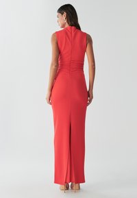 Rød, ærmeløs kjole med tætsiddende silhuet, samling på ryggen og en sideslids. Glat, strækbar stof komplimenterer designet.