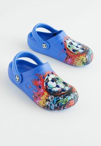 Kék crocs, színes, grafikás focilabdás dizájnnal, textúrált talppal és nagy szellőzőnyílásokkal. Fekete-fehér gomb részlettel rendelkezik.