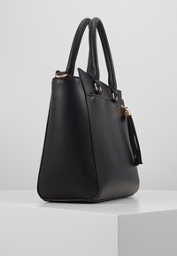 Borsa a mano in pelle nera con un design strutturato, dotata di hardware dorato, doppio manico e un accent decorativo in frange nere.