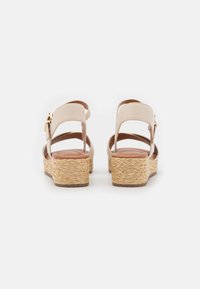 Sandales compensées beiges avec un dos ouvert, sangle ajustable, plateforme en jute tressé et tige en cuir lisse. Semelle plate avec une légère texture.