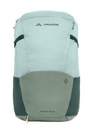 Hellblauer Rucksack mit grauen Akzenten. Hat eine glatte Textur, einen Reißverschluss oben und verstellbare Träger. "Skomer Zip 22"-Label sichtbar.