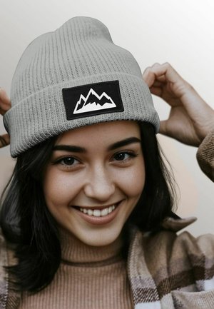 Gray knit beanie with a black patch displaying a white mountain design. The hat features a ribbed texture and a snug fit.