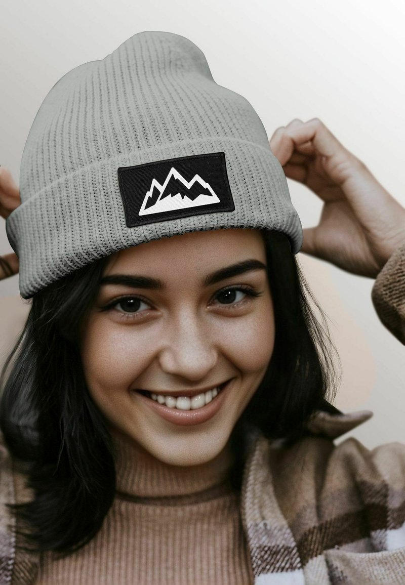 Gray knit beanie with a black patch displaying a white mountain design. The hat features a ribbed texture and a snug fit.