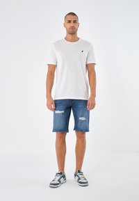 White short-sleeve shirt with a round neckline, paired with distressed blue denim shorts and grey sneakers with black accents.