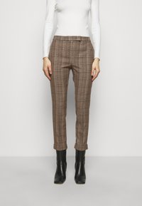 Pantalon à carreaux marron, coupe slim, avec une taille plate et des ourlets retroussés, associé à des bottines noires et un haut à manches longues blanc.