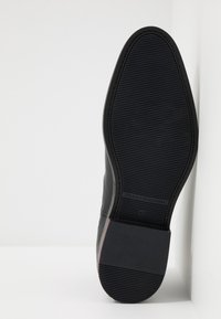 Suela de zapato de cuero negro con textura estriada, que presenta un tacón plano y redondeado, y un logotipo cerca de la base. Talla 42 marcada en la parte inferior.