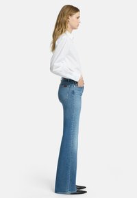 Jasnoniebieskie dzwony z denimu, z wysokim stanem, tylnymi kieszeniami i gładką fakturą. W połączeniu z białą koszulą z długim rękawem.