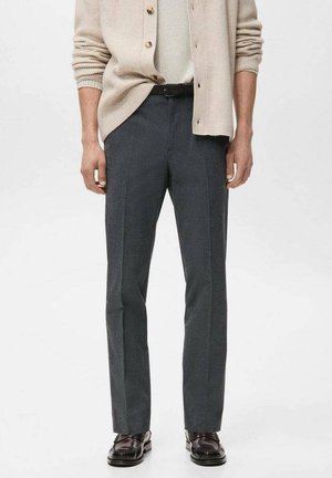 Pantalon en mélange de laine gris avec une finition texturée, coupe droite et plis avant soigneusement repassés. Associé à un cardigan beige.