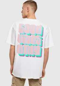 Hvid bomuld t-shirt med en stor, multifarvet grafisk tekst "Good Vibes Only" i fede, lagdelte skrifttyper på bagsiden.