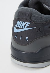 Gros plan sur le talon d'une basket Nike Air noire et grise avec un logo Nike bleu clair et une silhouette Jumpman sur un panneau texturé.