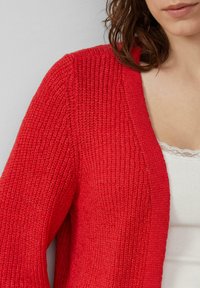 Rode gebreide cardigan met een V-hals en een open voorkant. Geweven materiaal met geribbelde details op de mouwen en het lichaam.