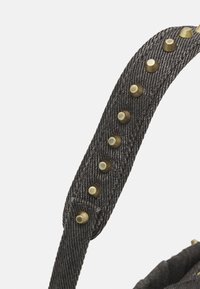 Sangle en denim noir avec de petits clous ronds en laiton espacés régulièrement sur un fond clair.