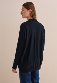 Cardigan bleu marine à coupe décontractée, avec des poignets et un empiècement côtelés, des manches longues, une texture lisse et un seul détail de couture au dos.
