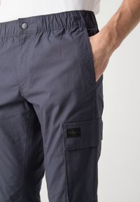 Námořnické cargo kalhoty s elastickým pasem, se bočními kapsami a nášivkou s logem na boku, vyrobené z lehkého materiálu.