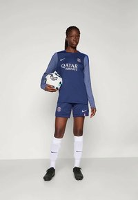 Tengerészkék foci mez szürke ujjal, logóval és "QATAR AIRWAYS" felirattal. Hozzá illő rövidnadrág, fehér zoknik és fekete focicipők. Foci labdát tart.