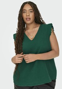 Top verde texturizado con escote en V y mangas con volantes. La tela tiene un aspecto ligeramente arrugado y un ajuste relajado.