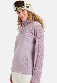 Lila Fleece-Pullover mit gemustertem Design, Halbreißverschluss-Kragen, Seitentaschen und Logo am Ärmel. Weicher Stoff mit enganliegender Passform.
