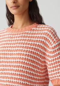 Pull en maille texturée avec un col rond, présentant des rayures alternées pêche et blanches, des manches courtes et une coupe loose.