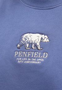 Sweatshirt azul com um urso branco bordado e o texto "PENFIELD", acompanhado dos detalhes "FOR LIFE IN THE OPEN" e "50TH ANNIVERSARY".