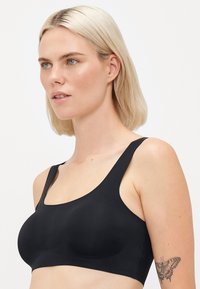 Svart sportsbh med brede stropper, en jevn tekstur og rund halslinje, med et minimalistisk design uten hardware eller detaljer.