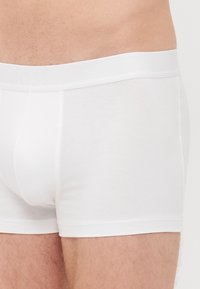 Boxers blancs en tissu doux avec une ceinture lisse embossée du nom de la marque "BOSS", présentant un design ajusté.