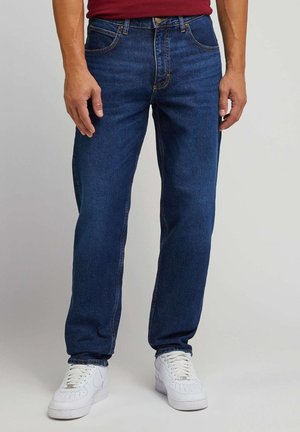 Dark blue denim jeans with a regular fit, five pockets, and visible stitching detail. Paired with white sneakers.