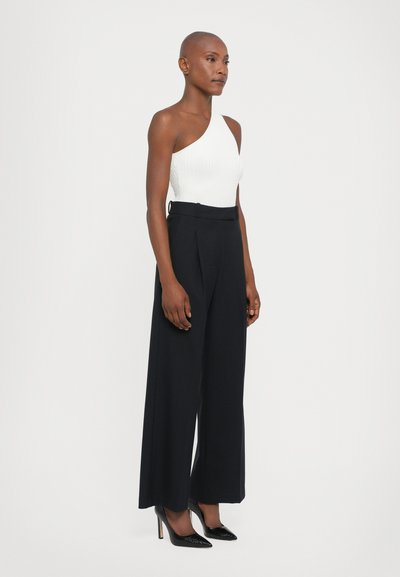 White ribbed one-shoulder top paired with high-waisted, wide-leg black trousers. Black high-heeled shoes complete the outfit.