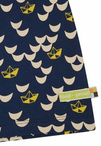 Tessuto blu navy con un motivo di barche gialle e onde color crema. Etichetta con "loud + proud" visibile lungo il bordo inferiore.
