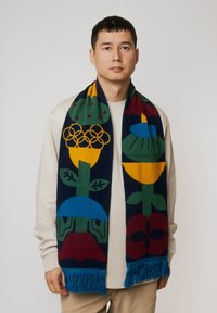 Dziany szalik z kolorowymi kwiatowymi wzorami w żółtym, zielonym, niebieskim i czerwonym na granatowym tle, wykończony niebieskimi frędzlami.