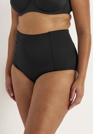 Person med kurver iført sort bikini-bund med høj talje og matchende bikini-top, stående mod en ensartet lys baggrund.